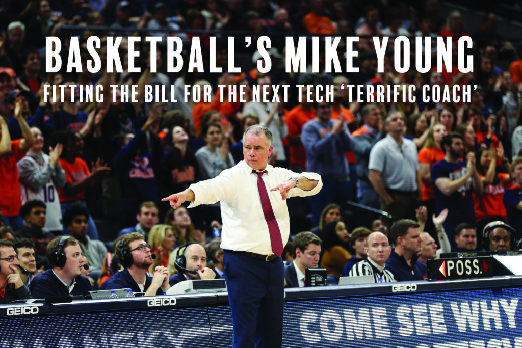 Coach in a white shirt and maroon tie points from the sideline during a game, with cheering fans behind him.