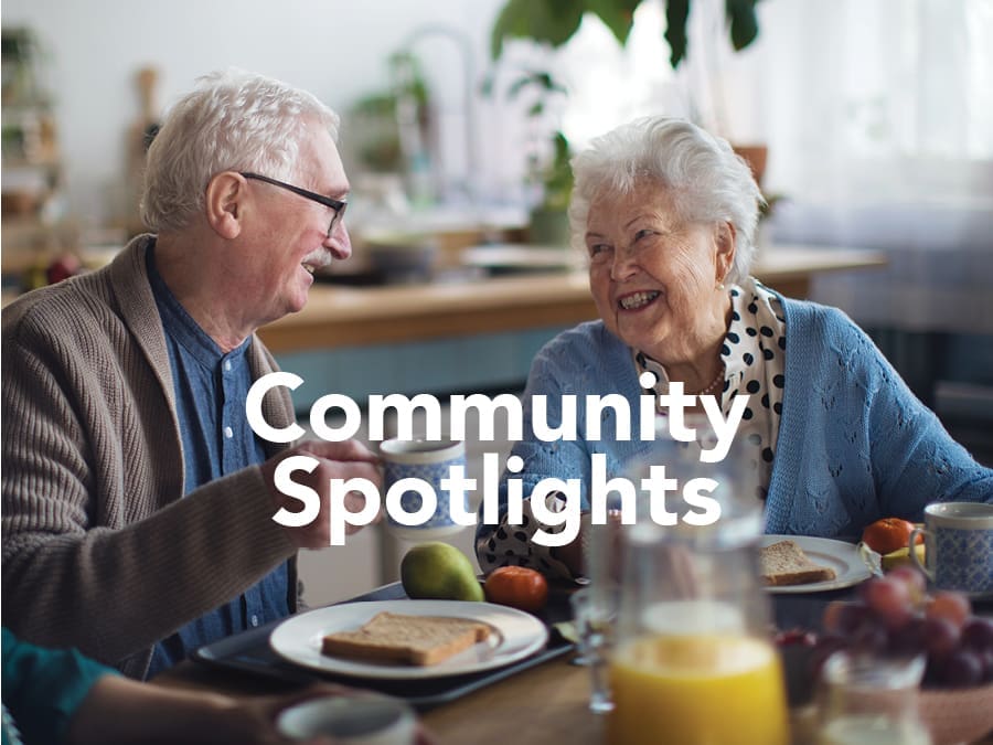 Two smiling older adults share a breakfast table with toast, fruit, and orange juice, with "Community Spotlights" overlaid.