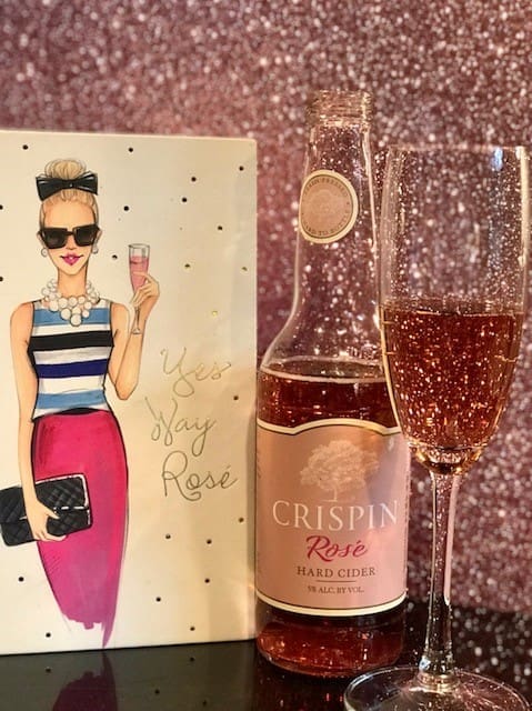 A bottle of Crispin Rosé hard cider beside a glass of sparkling rosé, with a card reading "Yes Way Rosé.