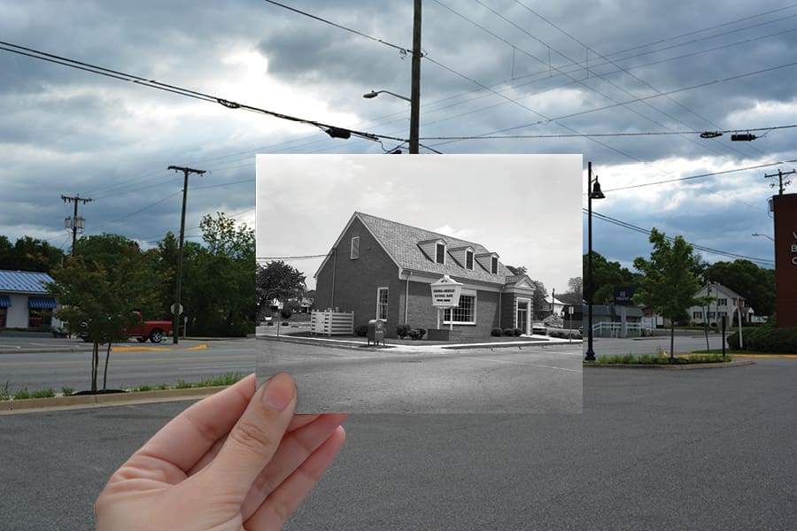 A hand holds a black-and-white print of a brick building over a present-day street scene.